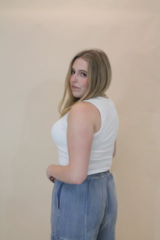 Person wearing a white tank top and blue jeans on a beige background