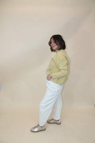 Person wearing a yellow hoodie and white pants standing on a beige floor.