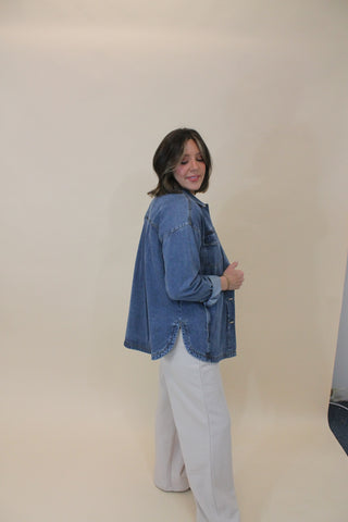 Person wearing a blue denim jacket and light gray pants against a plain background