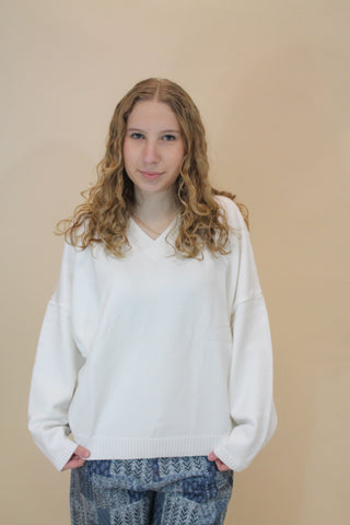 Woman wearing a white sweater and blue jeans against a beige background