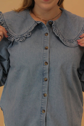 Close-up of a blue denim dress with buttons on a beige background