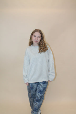 Person wearing a light gray sweater and blue jeans on a beige background