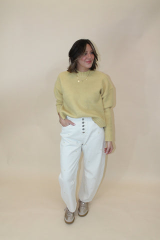 Person wearing a yellow sweater and white pants on a beige background