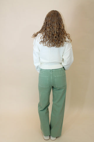 Person wearing green pants and a white puffer jacket on a beige background