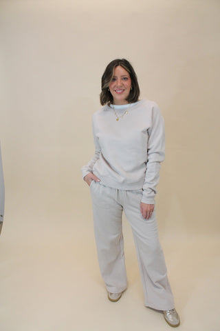 Person wearing a light gray hoodie and jeans on a beige floor.