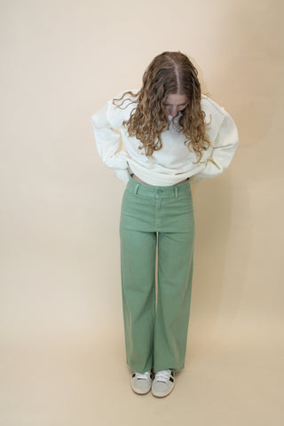 Person wearing a white blouse and green pants on a beige background