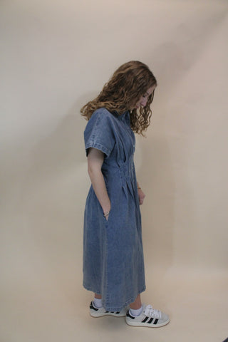 Person wearing a denim dress and Adidas shoes on a plain background