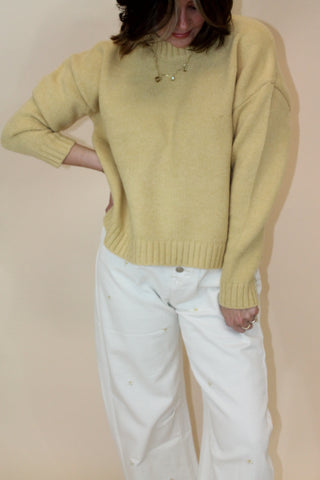 Person wearing a yellow sweater and white pants on a beige background