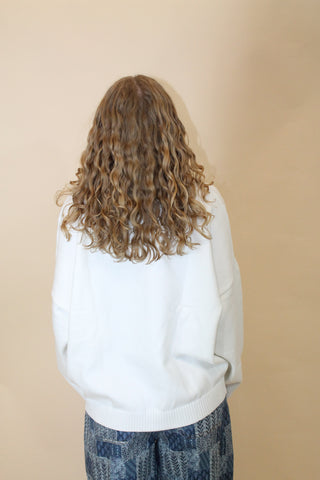 Person wearing a white hoodie and blue jeans with curly hair on a beige background
