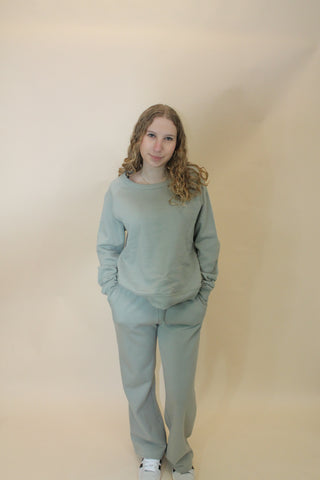 Person wearing a light green outfit standing against a beige wall.