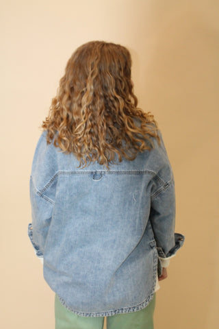 Person wearing a denim jacket from an overhead perspective on a beige background