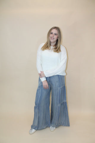 Person wearing a white sweater and blue jeans on a beige background