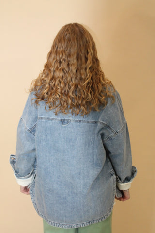Person wearing a denim jacket from an overhead perspective on a beige background
