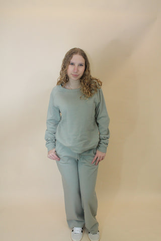 Person wearing a light green outfit standing against a beige wall.