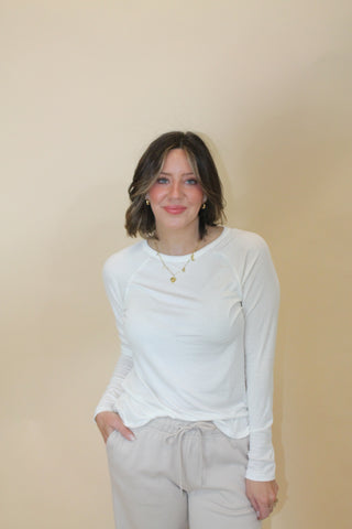 Person wearing a white long-sleeve shirt and light-colored pants on a beige background