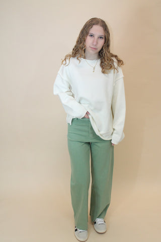 Person wearing a white sweater and green pants on a beige background