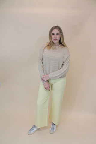 Person wearing a light gray sweater and light green pants on a beige background